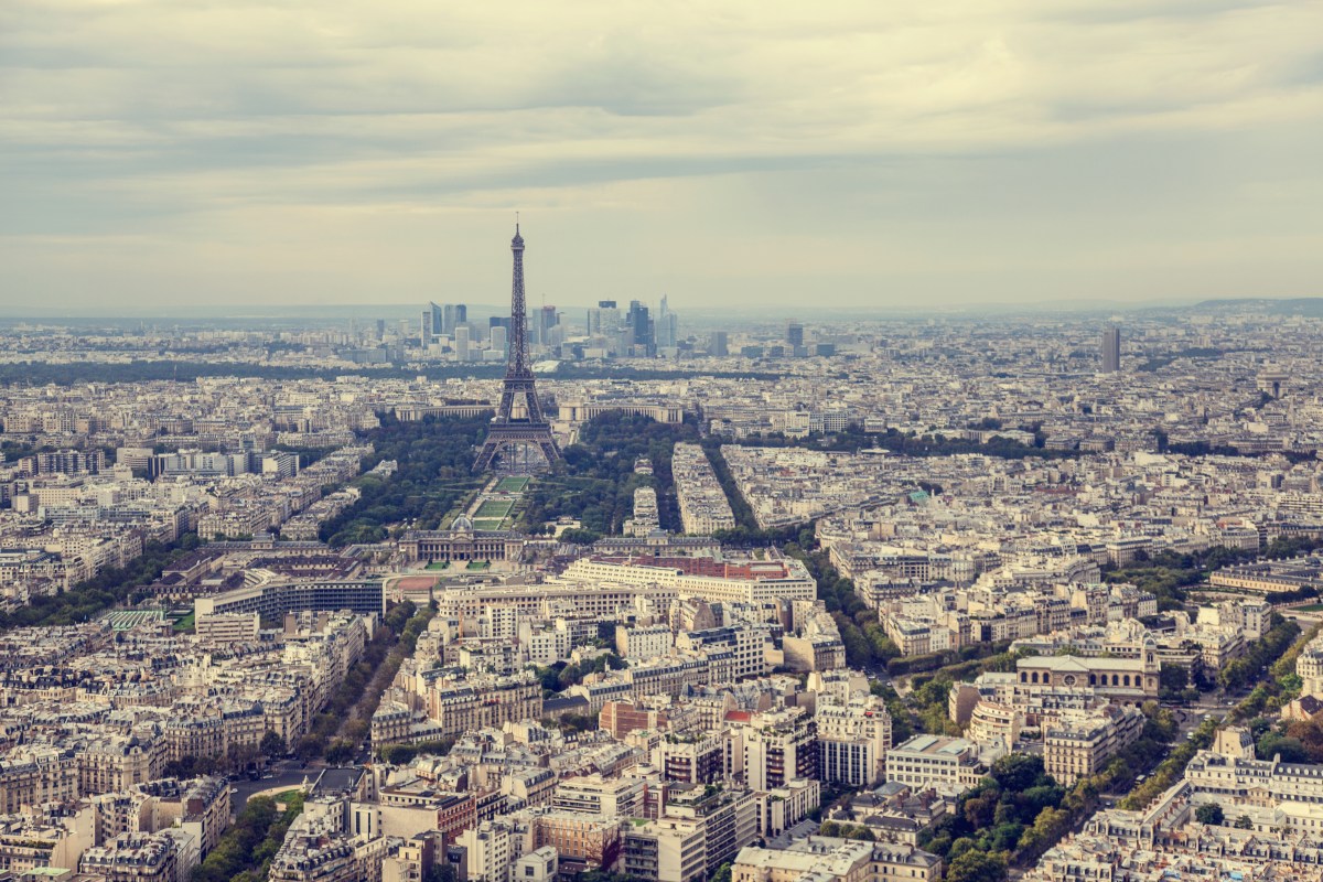 En flygbild över Paris; kvarter av hus och gator med Eiffeltornet i centrum, och en grå himmel.